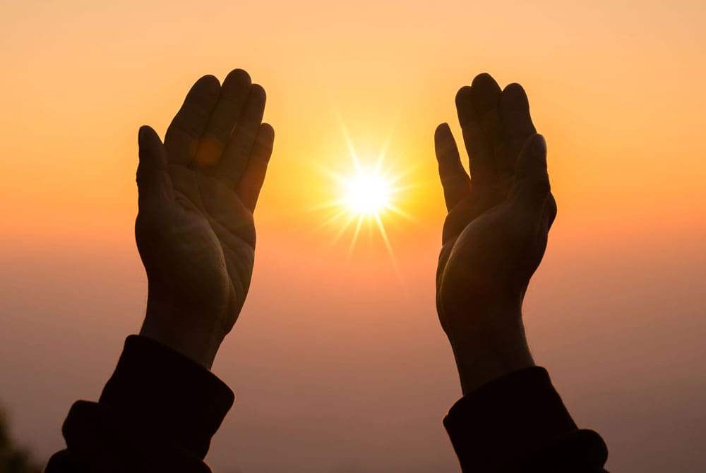 shadowed hands held up around the sunset